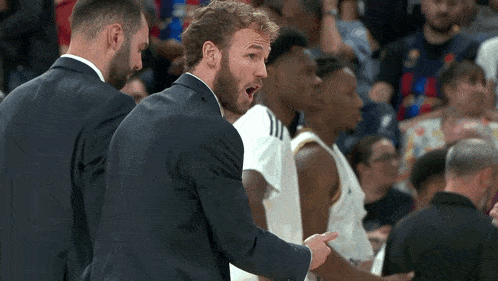 a man in a suit talks to a basketball player on the court