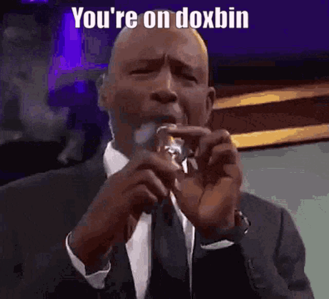 a man in a suit is drinking from a glass with the words `` you 're on doxbin '' written on it .