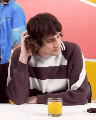 a man in a striped shirt sits at a table with a glass of orange juice