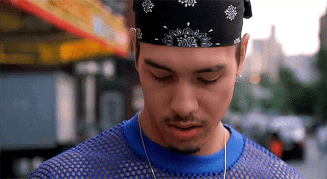 a man wearing a bandana and a blue shirt is looking down at something .