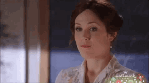 a woman is standing in front of a window wearing a white shirt and pearl earrings .