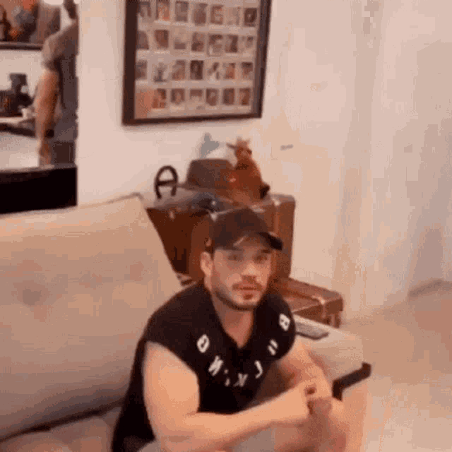 a man is sitting on a couch in a living room with a picture on the wall behind him