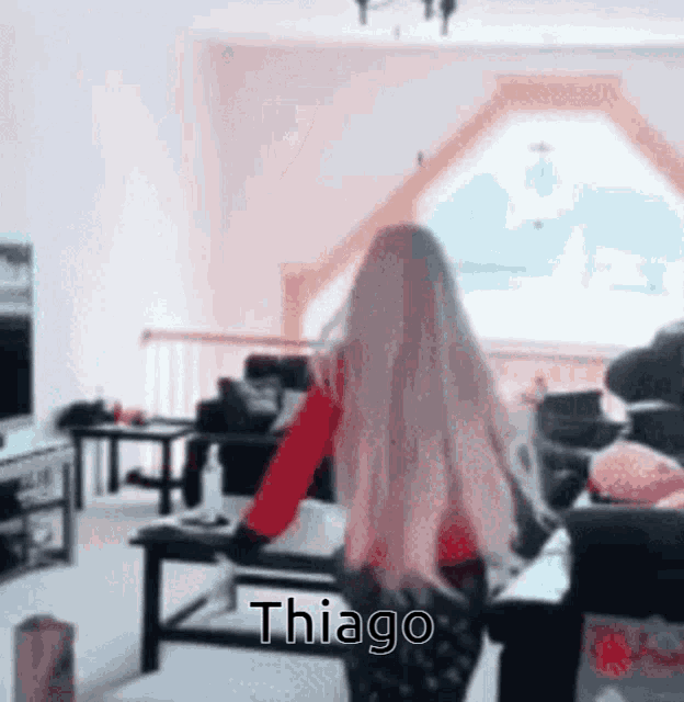 a woman with long blonde hair is standing in a living room with the name thiago written on the bottom of her back .