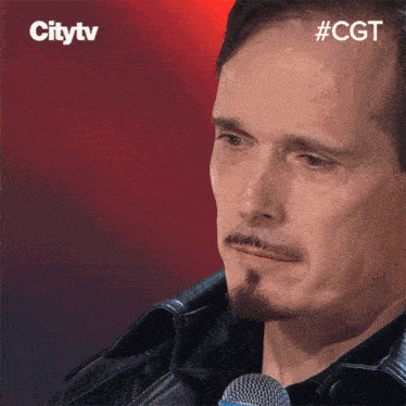 a man with a beard stands in front of a microphone and a citytv logo