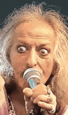 a close up of a woman singing into a microphone with her eyes wide open
