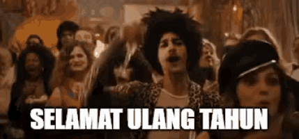 a man in an afro wig is standing in front of a crowd of people and says selamat ulang tahun .