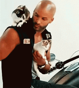a man is holding two cats on his shoulder while riding a motorcycle .