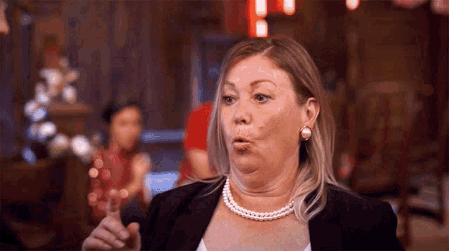 a woman wearing a pearl necklace and earrings is making a face