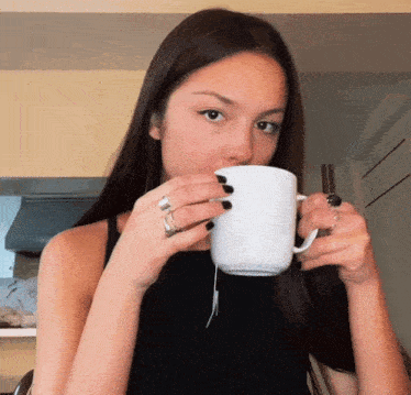 a woman is drinking from a white mug with a tea bag in it