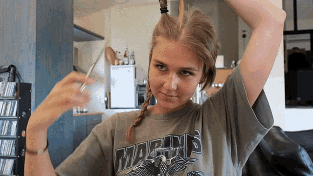 a girl wearing a shirt that says marines is cutting her hair