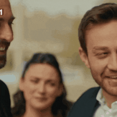 a man with a beard is smiling while a woman looks on