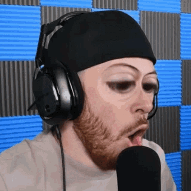 a man with a beard wearing headphones and a hat is singing into a microphone .