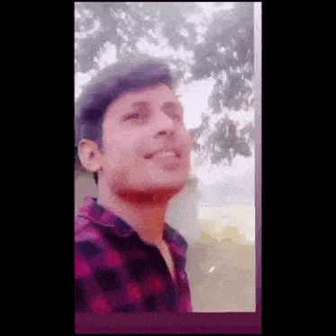 a young man in a plaid shirt is smiling and looking up at the sky .