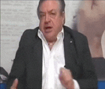 a man in a suit and white shirt is talking in front of a wall .