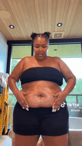 a woman in a black top and shorts is standing in a bathroom .