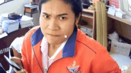 a woman wearing an orange jacket with a blue collar has a sign in the background that says " no front "