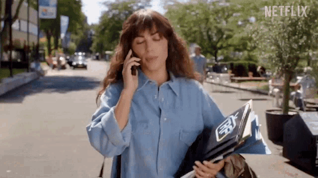 a woman is talking on a cell phone while holding a book and a newspaper .