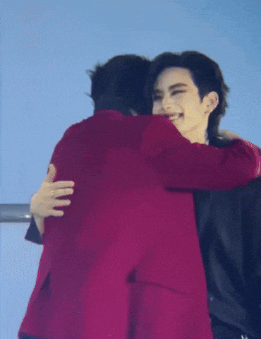 a man in a red jacket is hugging another man in a black suit