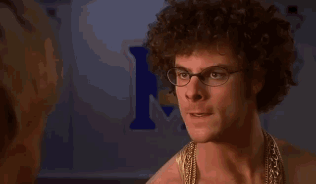 a man with curly hair and glasses stands in front of a sign that says m.