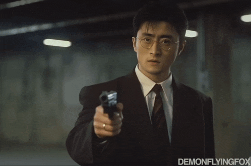 a man in a suit and tie is pointing a gun at the camera with the caption " avada katana "