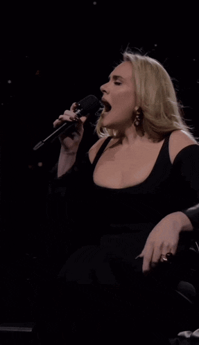 a woman singing into a microphone in a black dress