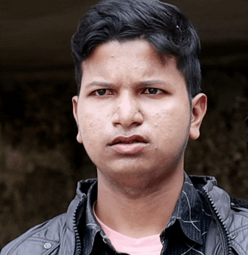 a young man wearing a black jacket and a pink shirt is looking at the camera