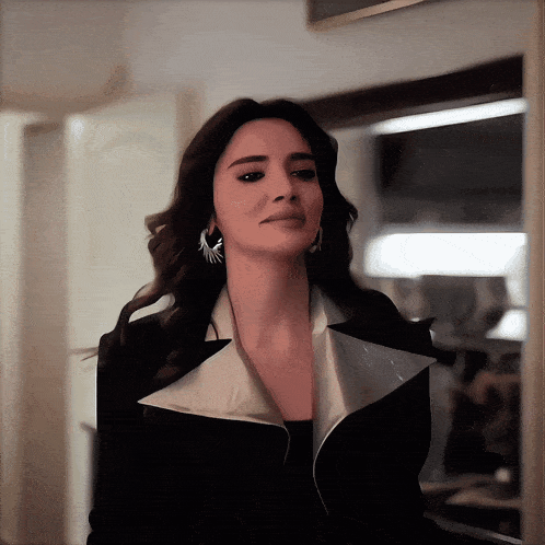 a woman wearing a black jacket and silver earrings looks at the camera