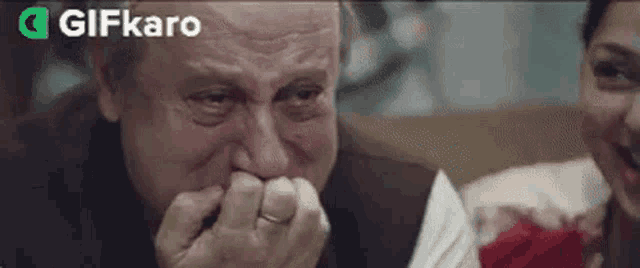 an older man is crying and covering his mouth with his hands while a woman laughs in the background .