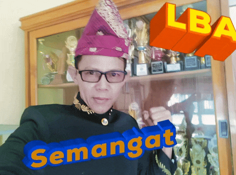 a man wearing glasses and a purple hat stands in front of a trophy case with the words semangat written in blue and orange