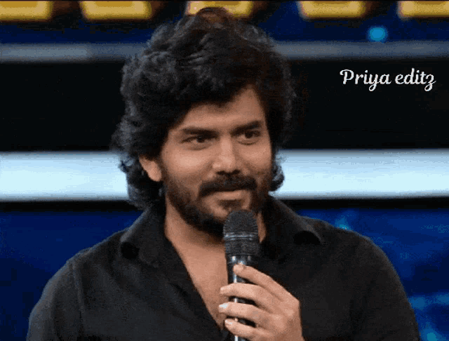 a man with a beard is holding a microphone and the name priya editz is on the bottom