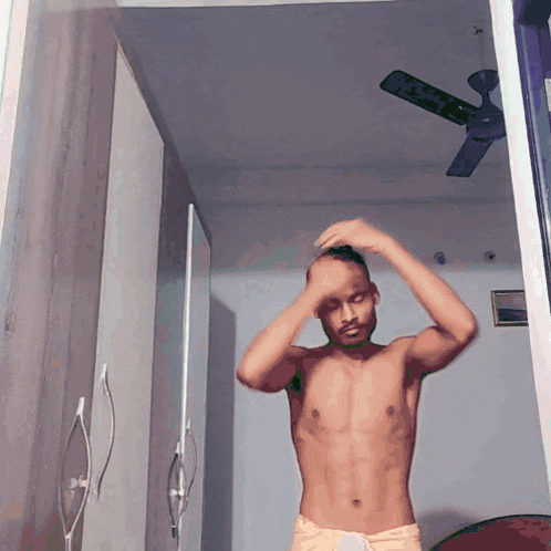 a shirtless man is standing in a room with a ceiling fan