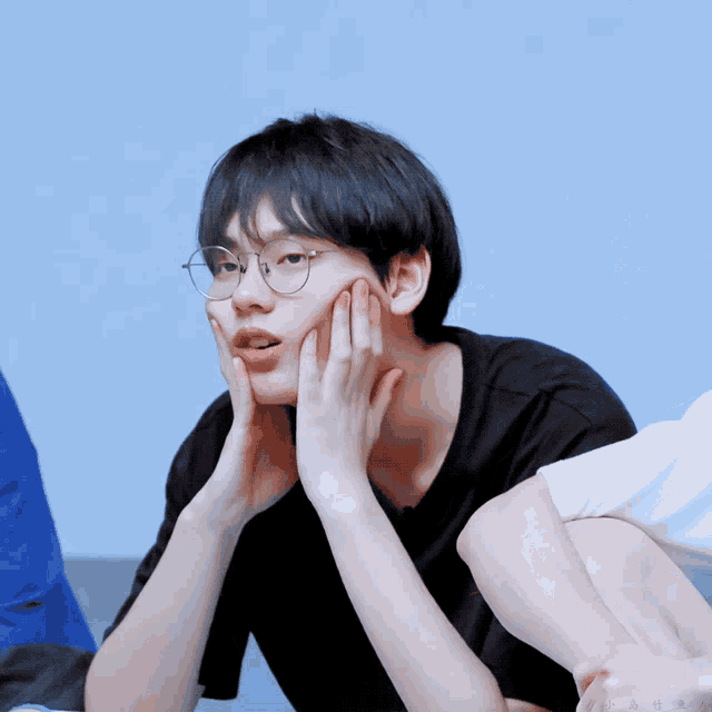 a young man wearing glasses and a black shirt has his hands on his chin