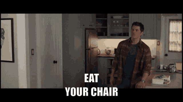 a man in a plaid shirt is standing in a kitchen with the words " eat your chair " on the screen