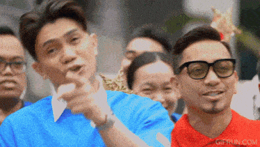 a man wearing glasses is pointing at something in front of a crowd with gifrun.com written on the bottom