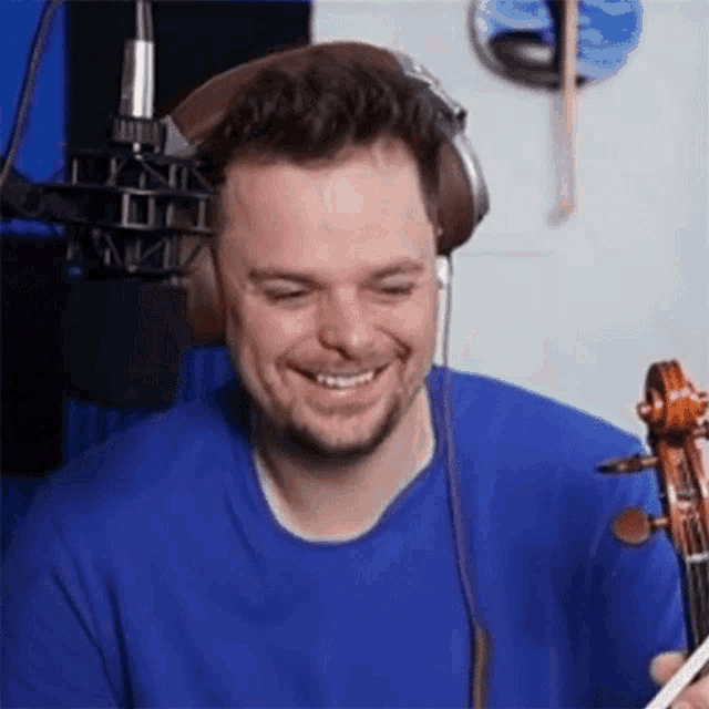 a man is wearing headphones and smiling while playing a violin in front of a microphone .