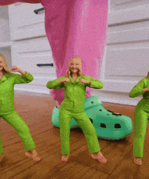 three women in green jumpsuits are dancing in front of a large croc