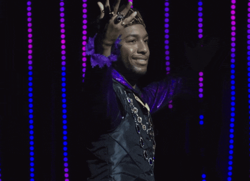 a man wearing a purple jacket and a gold crown stands in front of purple lights