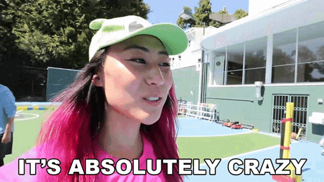 a woman with pink hair is wearing a green hat and says it 's absolutely crazy