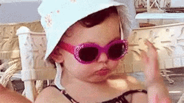 a little girl wearing sunglasses and a hat is giving the peace sign .