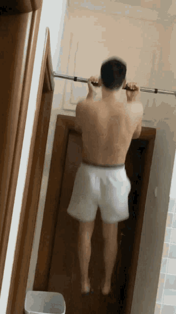 a shirtless man in white shorts is doing a pull up on a bar