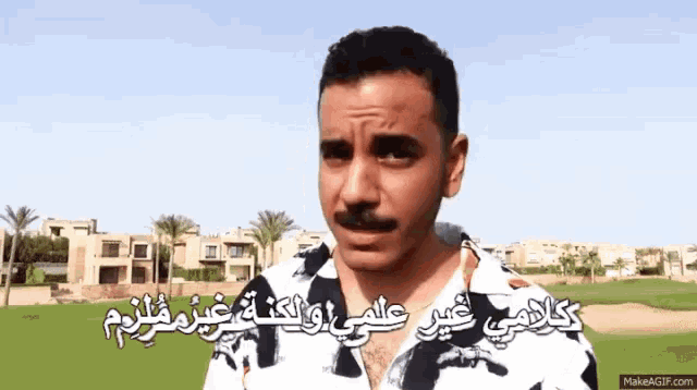 a man with a mustache is standing in front of a golf course with arabic writing on it .