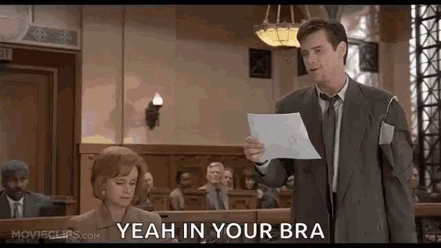 a man in a suit and tie is holding a piece of paper in a courtroom and talking to a woman .