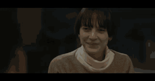 a woman wearing a sweater and a white turtleneck is smiling