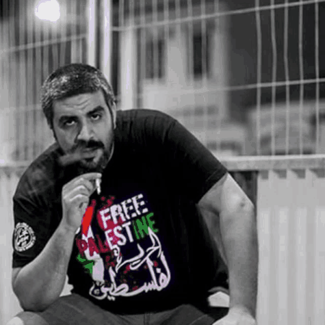 a man is smoking a cigarette while wearing a free palestine shirt .
