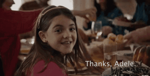 a little girl is sitting at a table with a plate of food and the words thanks adele .