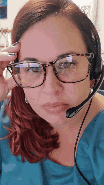 a woman wearing glasses and a headset holds her hand to her head