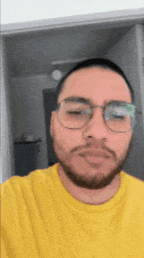 a man wearing glasses and a yellow shirt is making a funny face