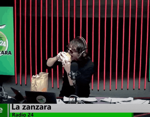 a man is eating a hamburger in front of a microphone at radio 24