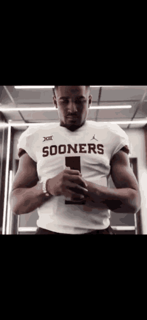 a man in a sooners jersey holds a cell phone