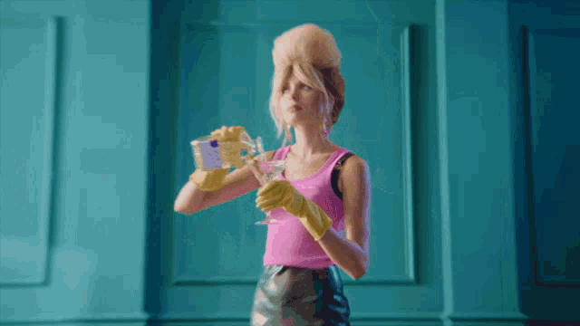 a woman wearing a pink tank top and yellow gloves is holding a martini glass